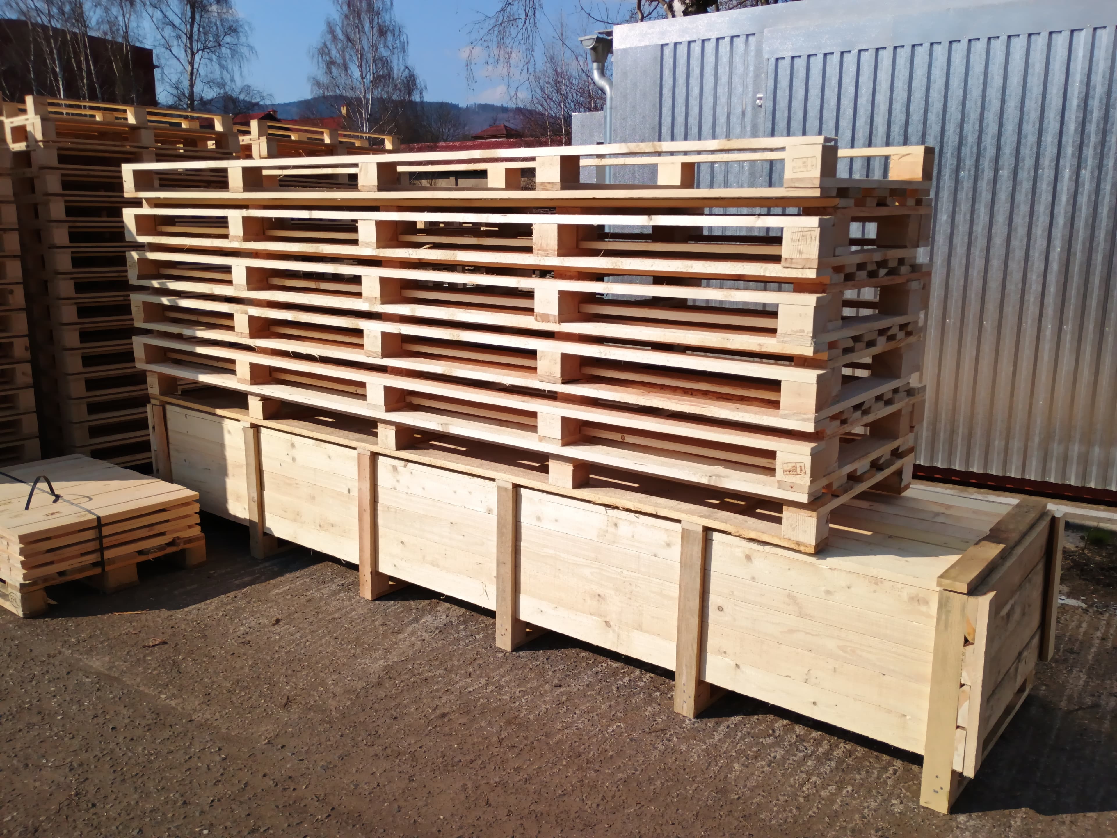 Stacked wooden pallets resting on a large wooden crate in an outdoor industrial yard.