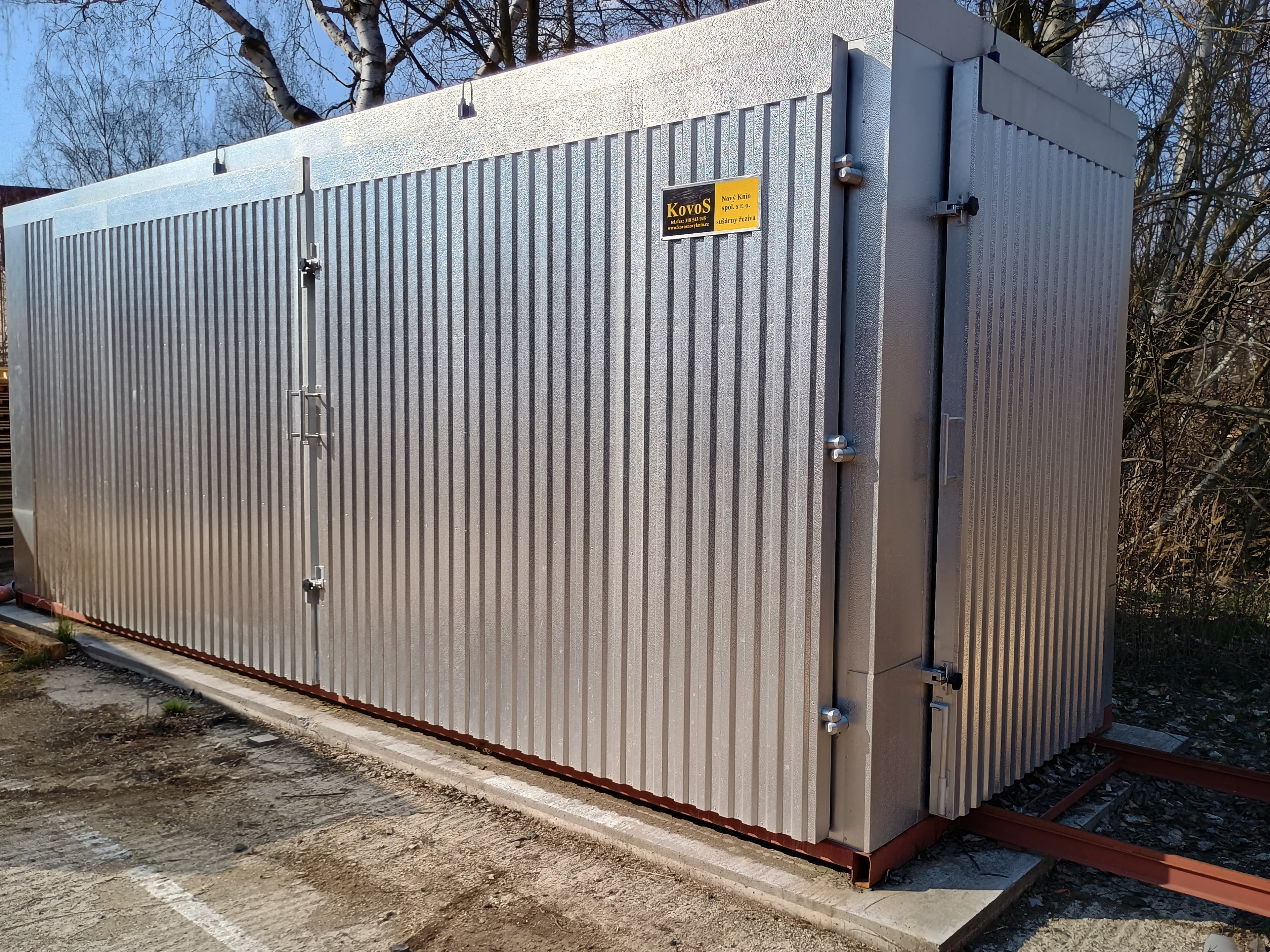 Large silver corrugated metal industrial unit with double doors, sitting on a concrete base outdoors.