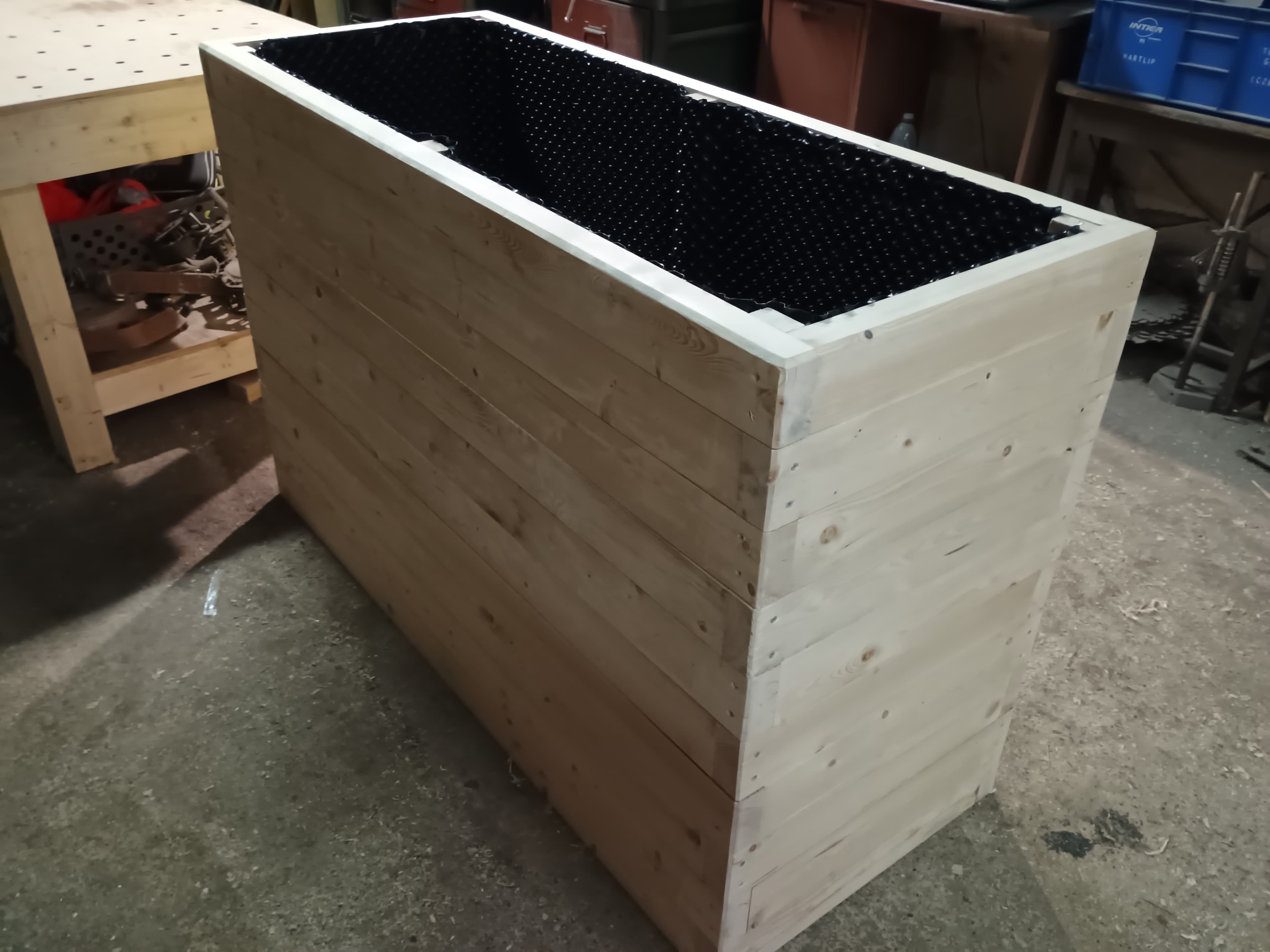 Large rectangular wooden planter box lined with black dimpled plastic in a workshop setting.